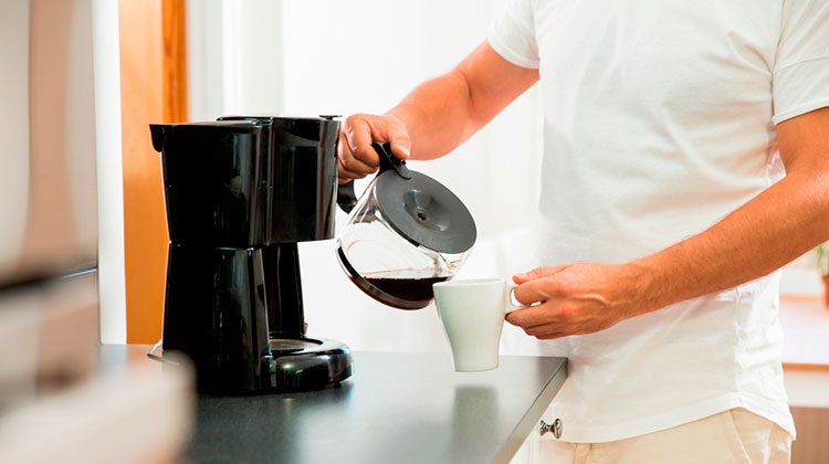 Person pouring coffee into their white mug from a coffee pot