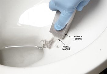Gloved hand using a pumice stone to scrub away scratches on a porcelain toilet bowl.