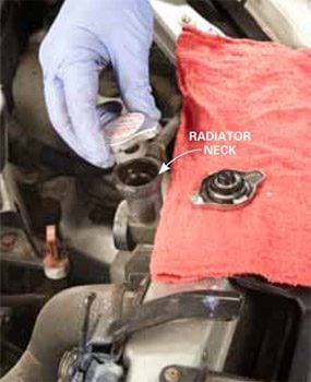 Radiator cap being replaced; old radiator cap is ling to the side on a rag.