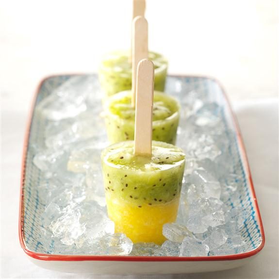 Frozen pineapple-kiwi pops in a row on a rectangular platter lined with crushed ice