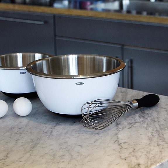 Black-handled balloon whisk beside two bowls on a metal counter