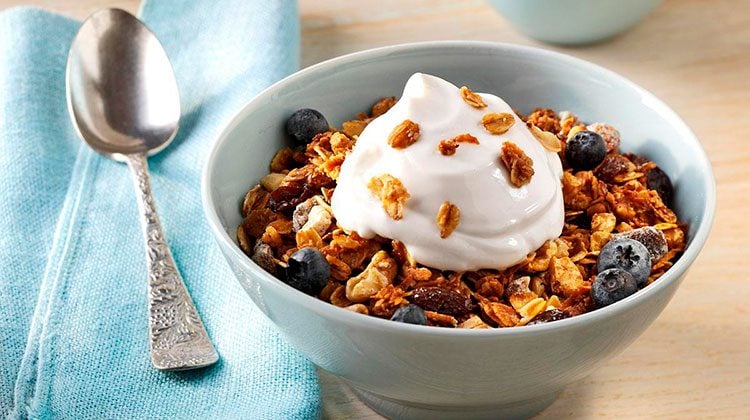 granola piled high in a light blue bowl mixed with blueberries and with whipped cream on top