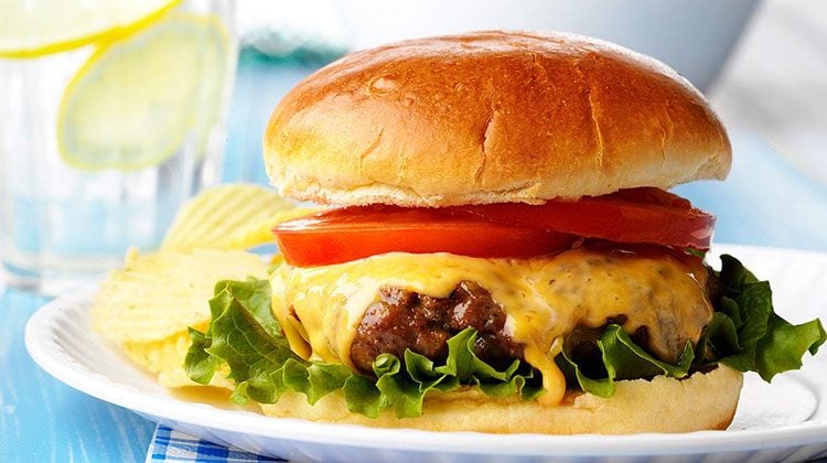 Cheeseburger with fixings on a white dish beside a large glass of lemonade