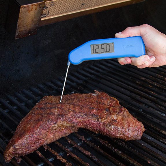 Blue thermapen being inserted into a piece of meat on the grill and getting a reading of 125.0 degrees fahrenheit