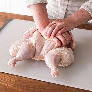 Person with one hand over the other pressing down down on the breast of the raw chicken