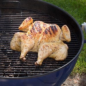 Spatchcocked chicken with black grill marks on its breast laying on a charcoal grill