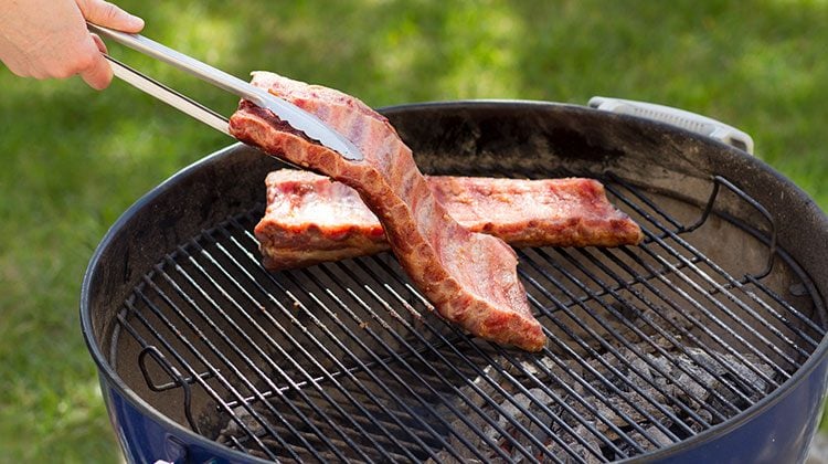 Person carefully placing their prepared ribs on the grill with metal tongs
