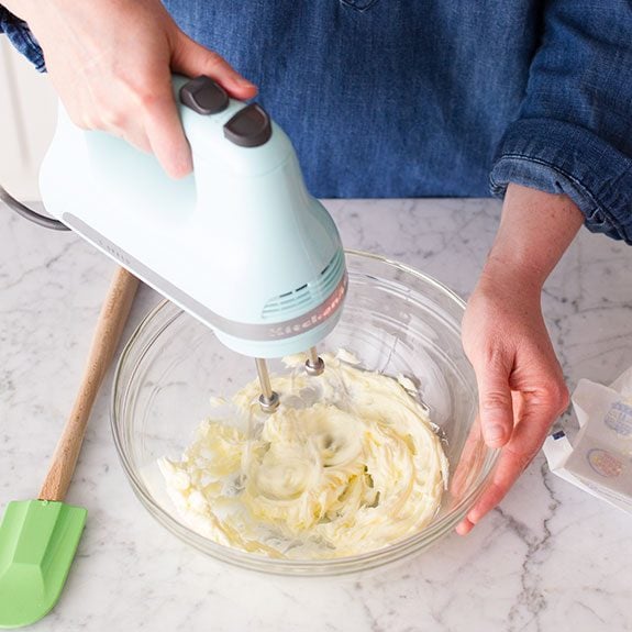 Person using a hand mixer to beat butter in a glass bowl