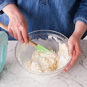Person using a spatula to scrape the dough off the sides of the glass bowl