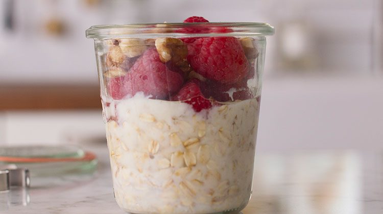 Oatmeal in a glass topped with raspberries and nuts