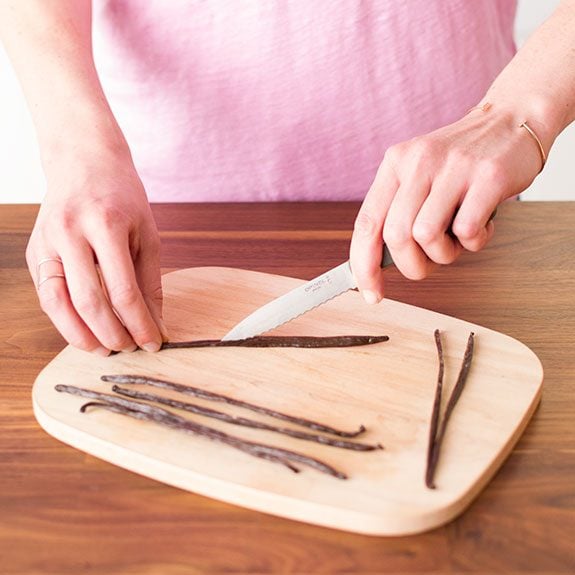 A knife being run along the middle of a vanilla bean to carefully expose the inner seeds