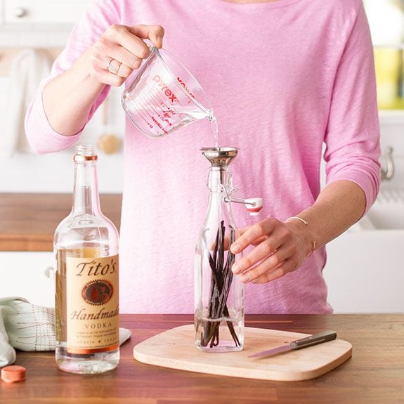 Alcohol is being poured into a bottle with several strands of vanilla beans inside
