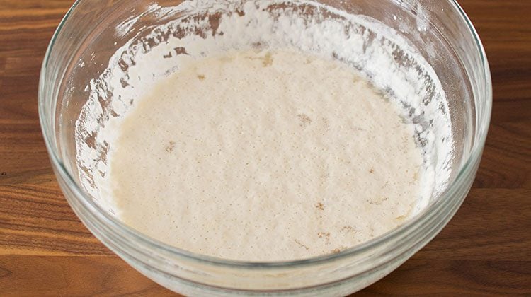 yeast mixture sits in a large glass bowl with bubbles peeking though its surface