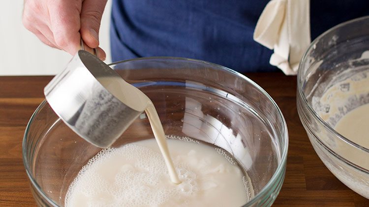 person pouring sourdough starter from a measuring cup into the mixture