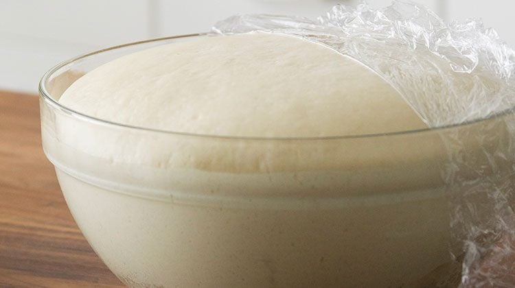 bread dough sits in a large glass bowl rising