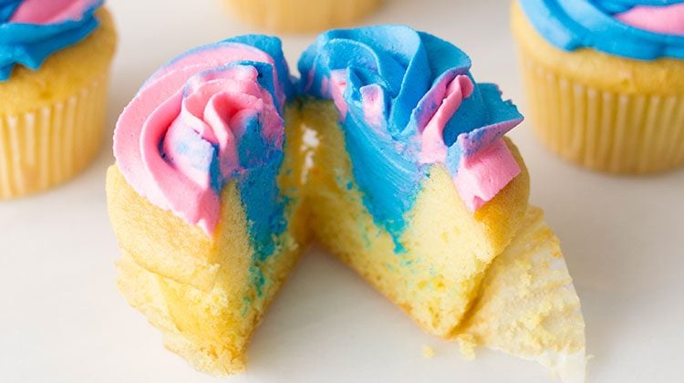 Three cupcakes with swirled pink and blue frosting with blue filling showing through one cut in half