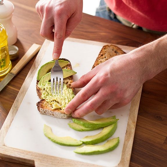 Person using a fork to mash slices of avocado on top of a piece of toast