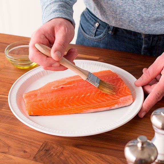 Person slathering a salmon with olive oil using a brush