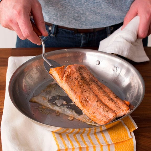 Person using a metal spatula to remove their salmon from the skillet, the skin of the fish being left behind as it sticks to the surface
