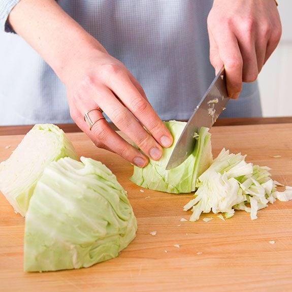 person using a knife to cut a wedge of cabbage into thin strips
