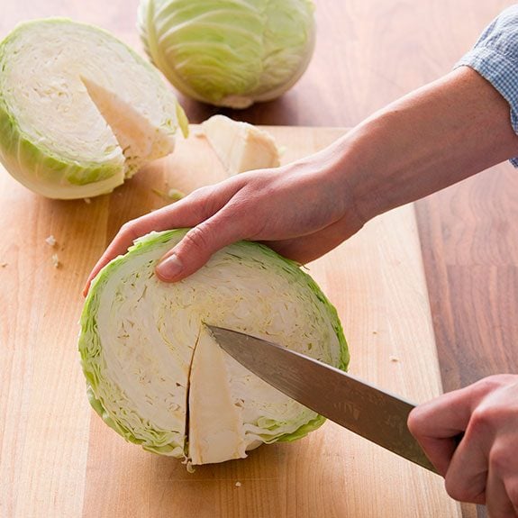 person cutting a v-shaped wedge out of a cabbage wedge with a knife