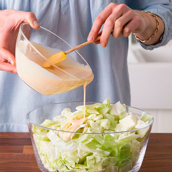 person pouring a vinaigrette over shredded cabbage