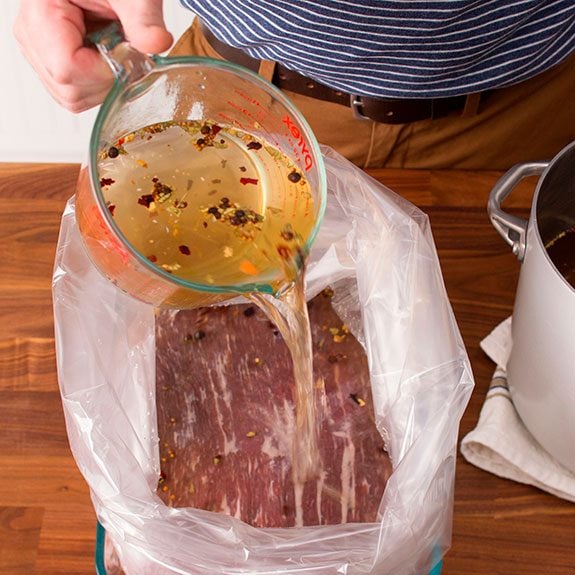 beef in an oven bag with brine being poured onto it from a measuring cup