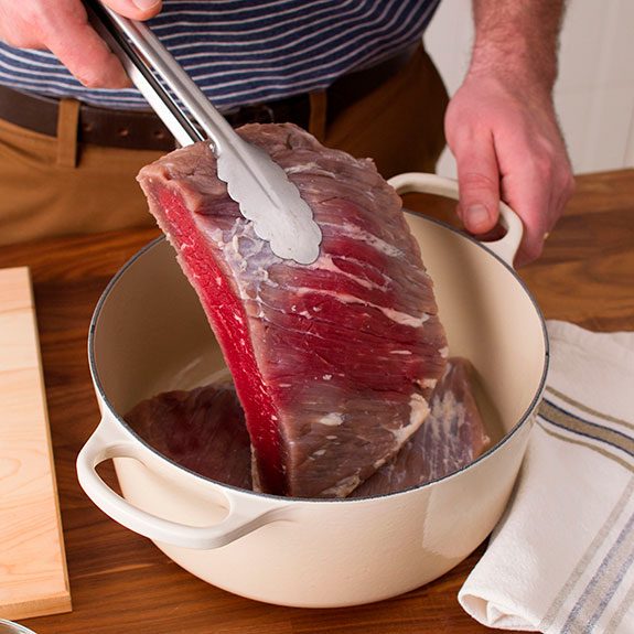 corned beef being turned over with tongs in a Dutch oven