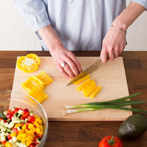 Person slicing a yellow pepper on a wooden cutting board