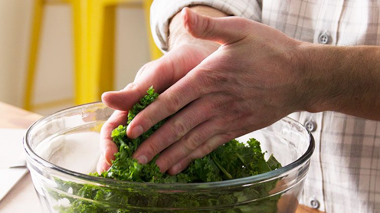 person massaging kale that is within a glass bowl