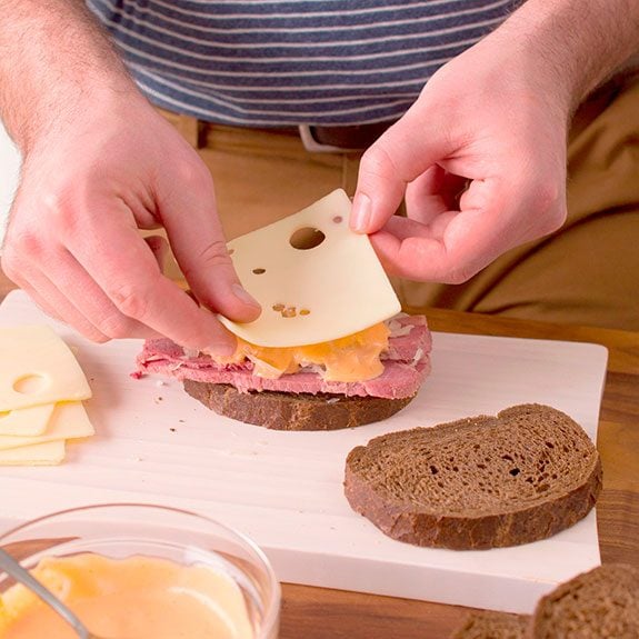 person laying slices of bread with cheese, meat, sauerkraut and sauce
