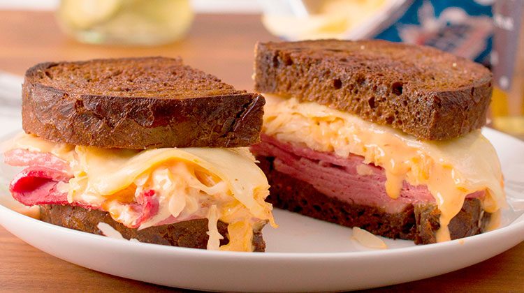 Reuben sandwich cut in half sitting on a plate with gooey cheese pouring over its sides