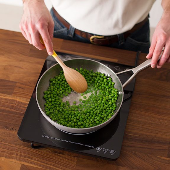 Person stirring peas in a skillet with a wooden spoon