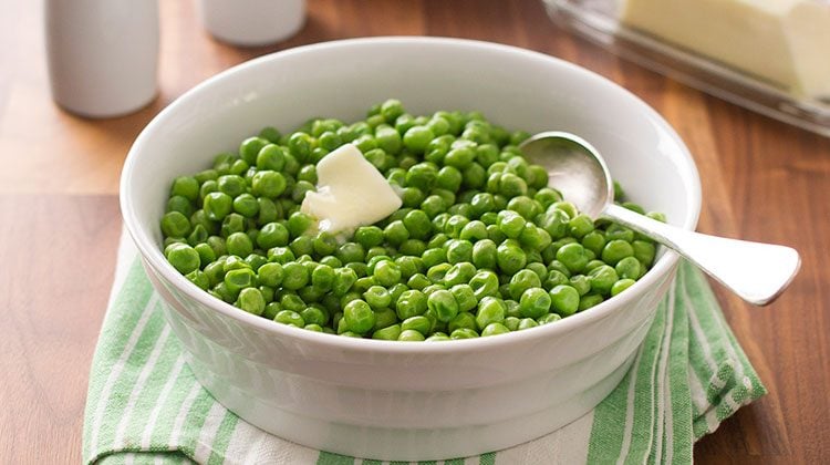 Hot, fresh peas piled high and topped with butter in a bowl