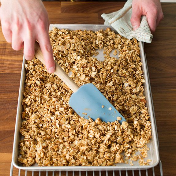 person spreading granola onto a baking sheet with a spatula