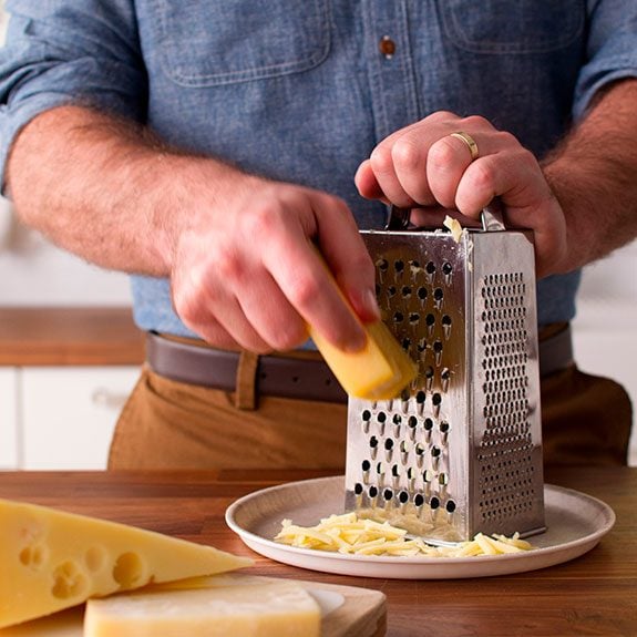 Person shredding cheese by hand with a grater, a pile of shreds are already building up below