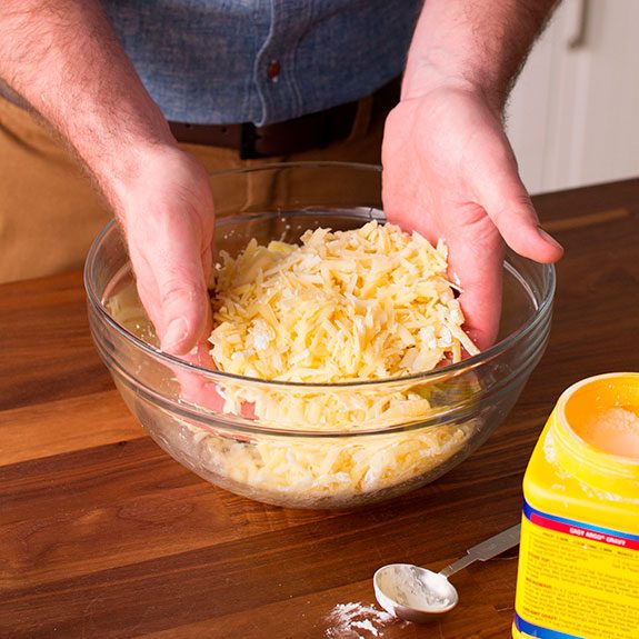 Person using their hands to mixture cheese with other ingredients together in a glass bowl