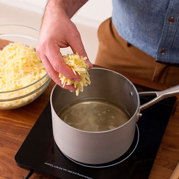 Person holding a handful of shredded cheese over a bowl of boiling water