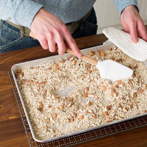 person stirring oats and almonds on a baking sheet with a spatula