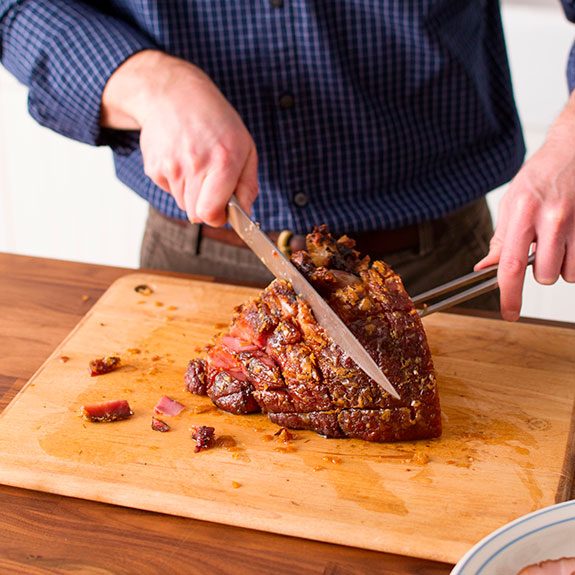 person cutting into the center of a cushion of ham meat with a fork embedded in the thickest part