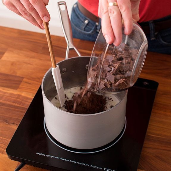 Person pouring solid chocolate pieces into a sauce pan on the stovetop