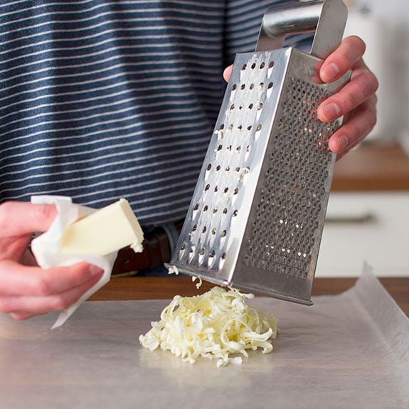 person shredding a stick of butter by rubbing it on a metal cheese grater