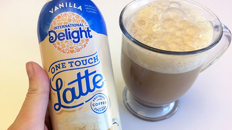 Bottle of International Delight Instant Latte beside a glass cup filled with foam and coffee