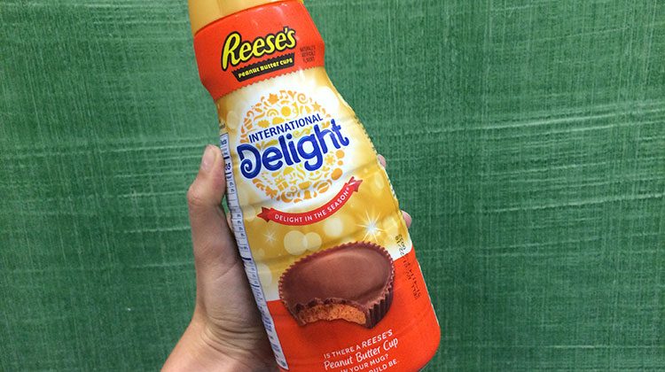 Hand holding a Reese's International Delight creamer with a picture of a Reese peanut butter cup with a bite out of it on the front