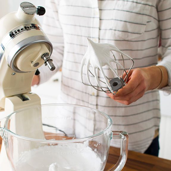 person pulling a whisk attachment out of a mixer with its bowl full of meringue