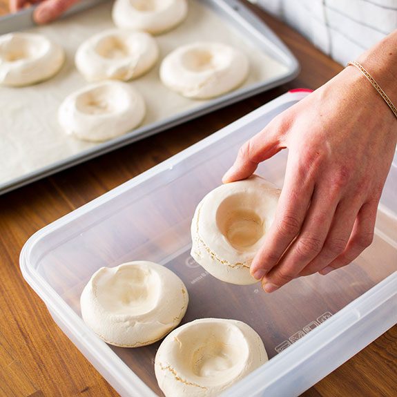 person putting the cooled meringue cups from the baking sheet into a tuber ware container