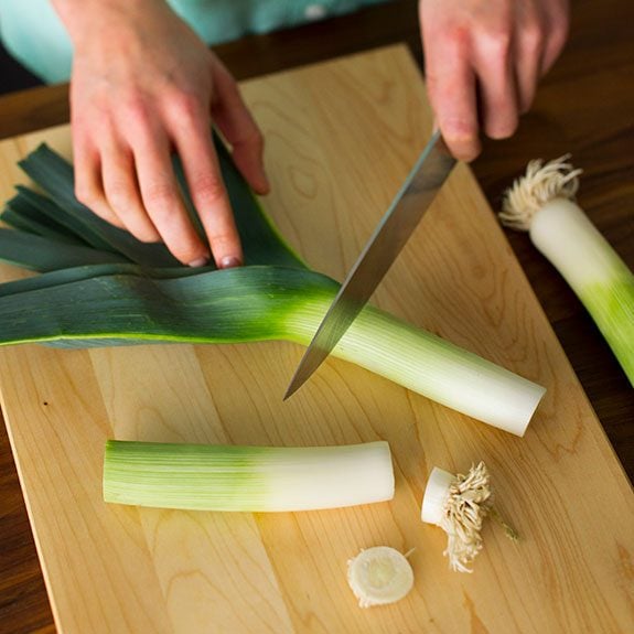 person slicing the ends off of several leeks using a knife