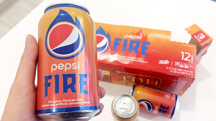 Can of Pepsi fire in hand being held over the cardboard 12 pack and other scattered cans