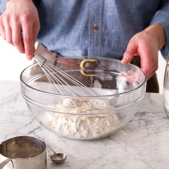 Person mixing dry ingredients together in a large glass bowl