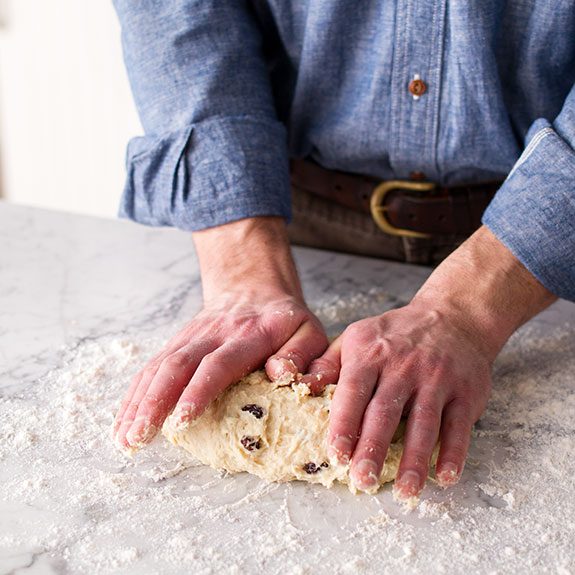 Person kneading soda bread dough out on a floured countertop